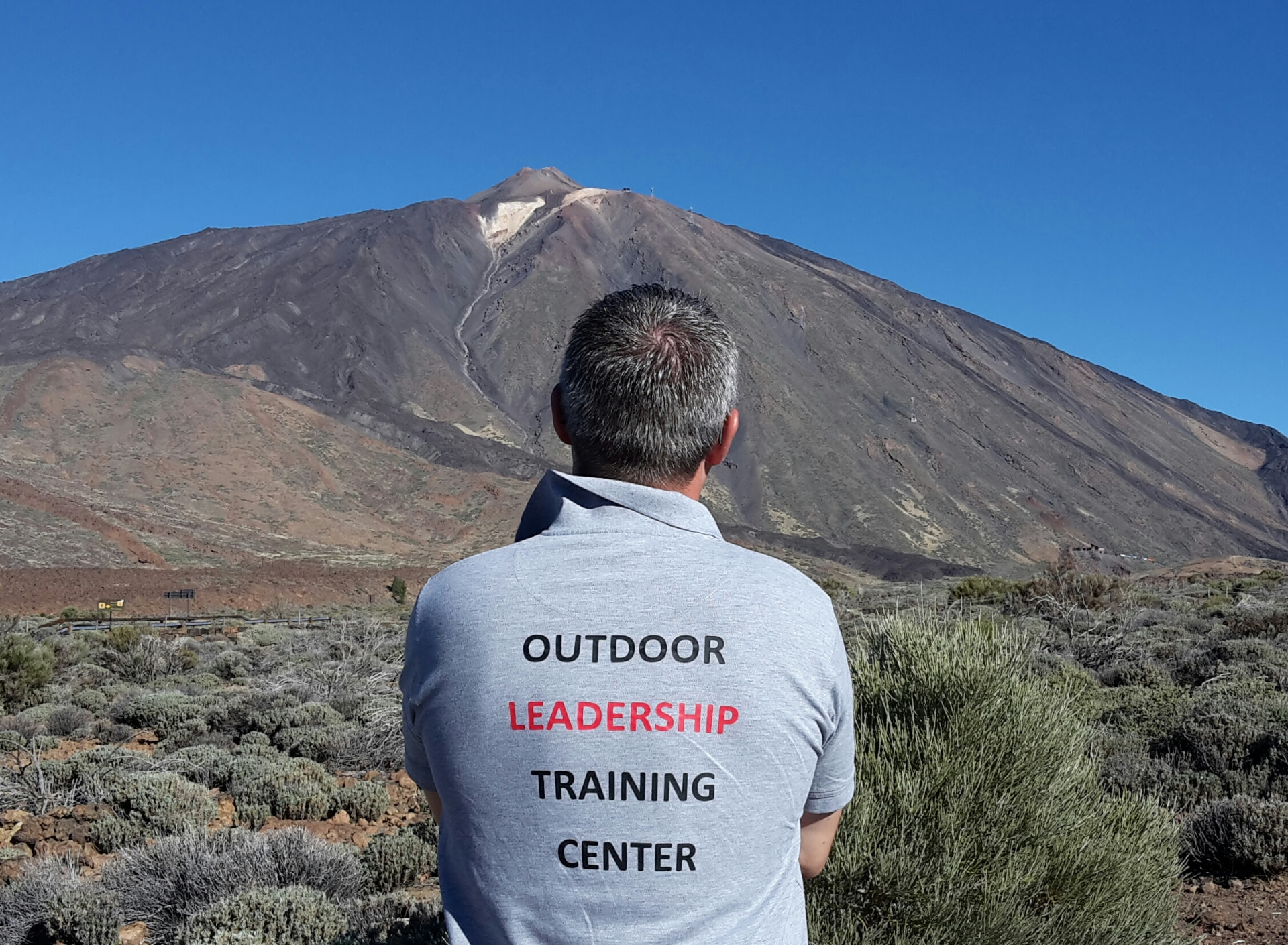 Mads Cronquist seen from behind in front of a mountain with Outdoor Leadership Training Center on his back