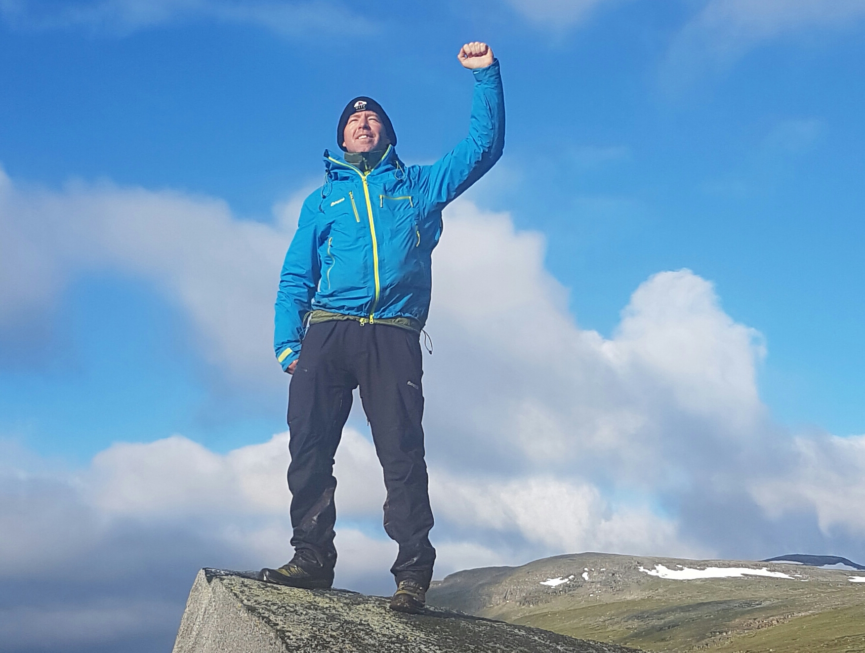 Mads Cronquist on a mountain top with his arm raised