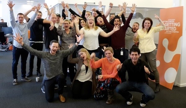 Glad gruppe e-conomic-medarbejdere med armene i vejret på kontoret foran et Getting Started-banner